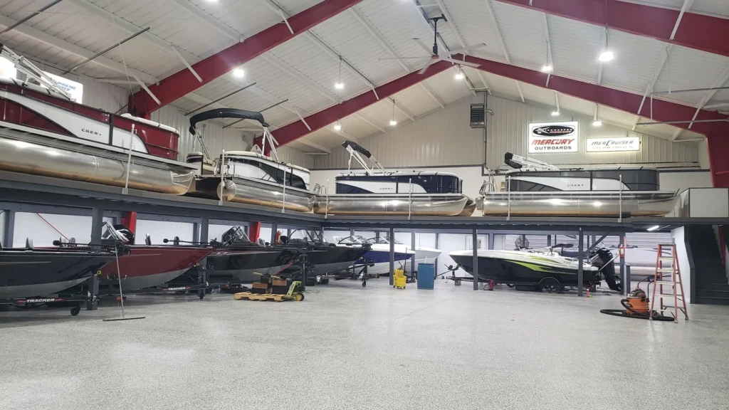 Indoor boat showroom featuring multiple boats on two levels, bright lighting, signs for Mercury Outboards, and a neatly organized, spacious interior.