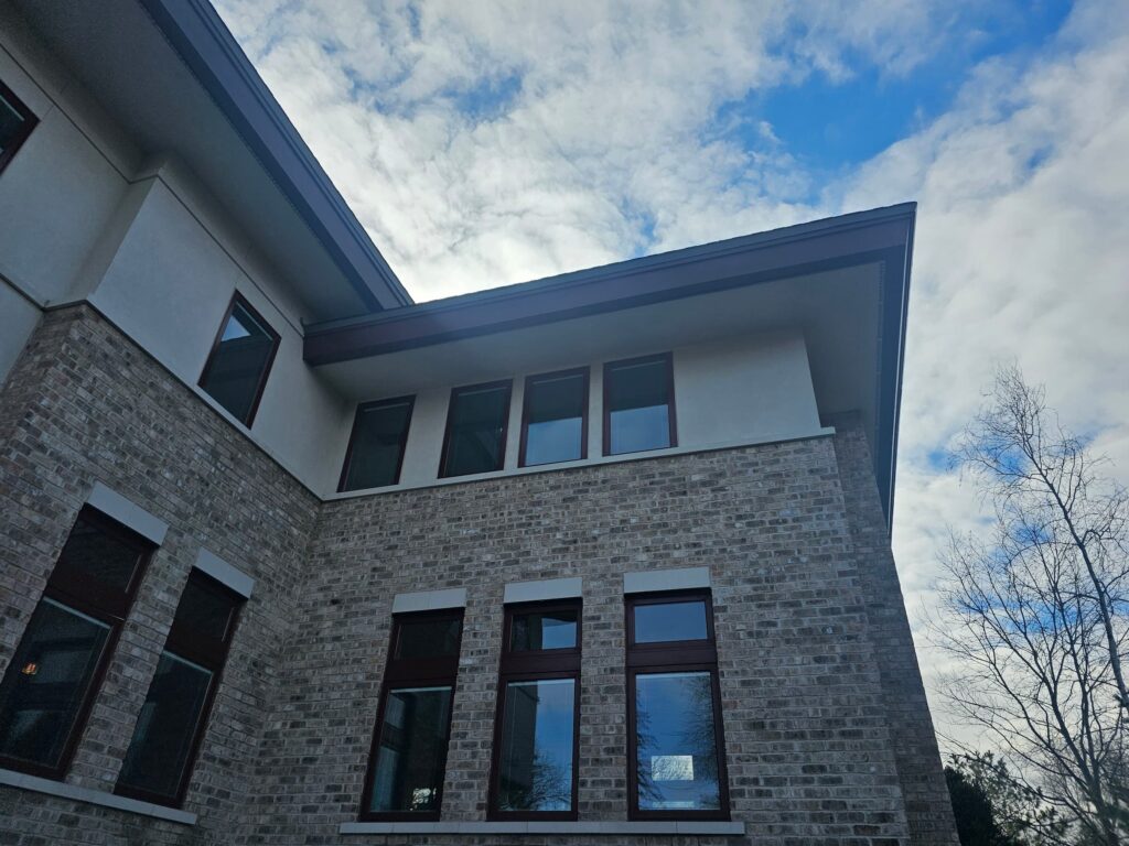 A modern brick building with large windows is set against a partly cloudy sky, and bare trees are visible beside it.